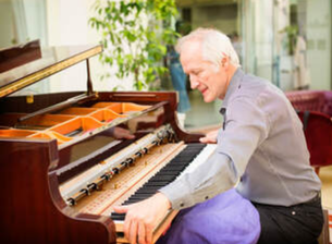 Picture of an elderly piano technician removing the keyboard of a grand piano ready to make repairs