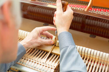 Picture of an elder piano technician softening the felt of a piano's hammers using a needle