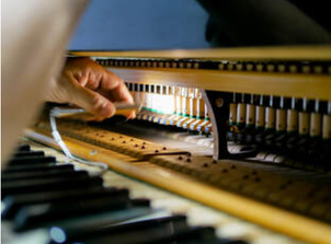 Picture of a technician repairing the mechanisms of a piano using a torch for extra light