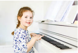 Picture of a smiling young girl sat ready to play a white upright piano