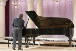 Picture of a piano mover examining a grand piano in a concert hall