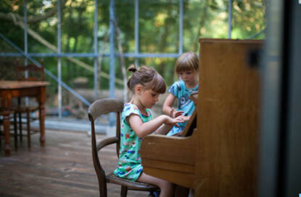 Picture of two young girls sat by a piano in a bright home environment, with one ready to play the piano