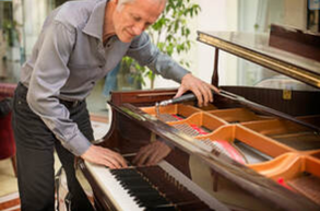 Picture of an elderly piano technician listening carefully as he tunes a grand piano