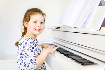 Picture of a young girl learning to play the piano and smiling at the camera